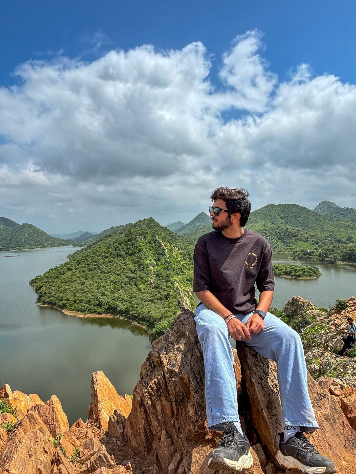 Panoramic view from Bahubali Hills in Udaipur, showing the tranquil blue waters of Badi Lake framed by the rugged Aravalli mountains at sunset.