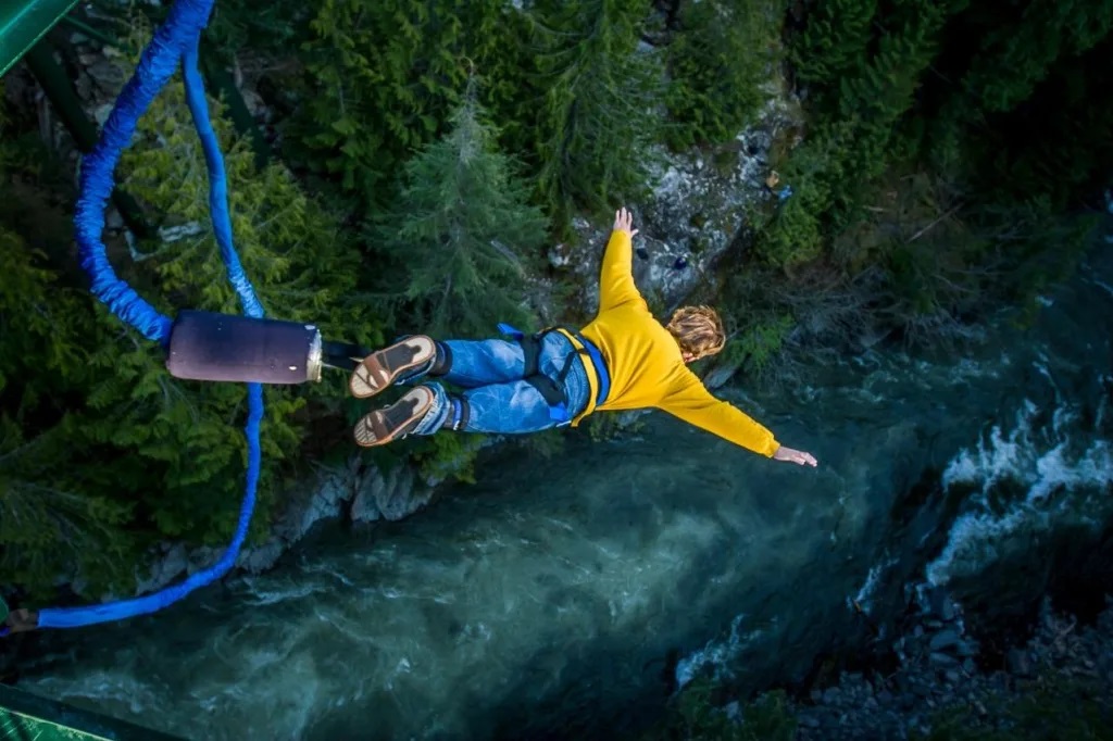A photograph of a person in mid-air, having just jumped from a bungee platform, with a scenic view of a valley and a river below.