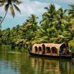 A traditional Kettuvallam (houseboat) cruising on the tranquil backwaters of Kerala, surrounded by lush tropical greenery, highlighting one of the top destinations in India.