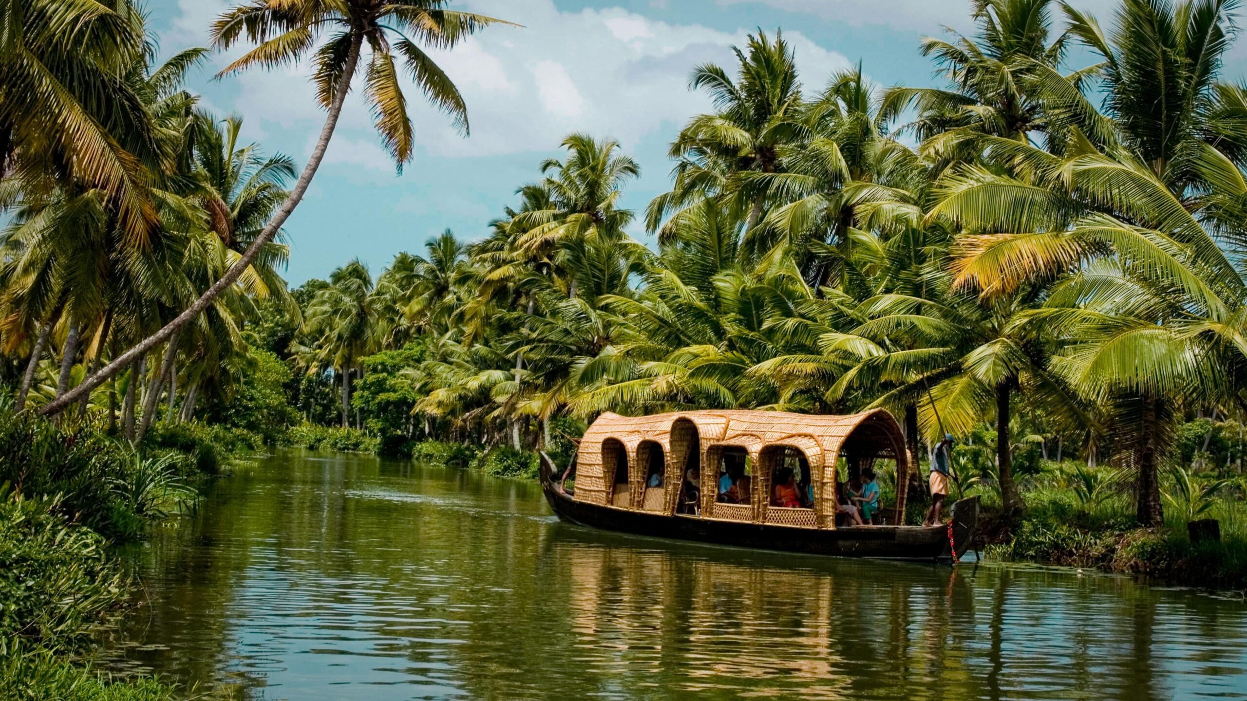 A traditional Kettuvallam (houseboat) cruising on the tranquil backwaters of Kerala, surrounded by lush tropical greenery, highlighting one of the top destinations in India.