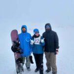 A snowboarder in the snow on a slope with a ski lift and mountains in the background at Gulmarg.