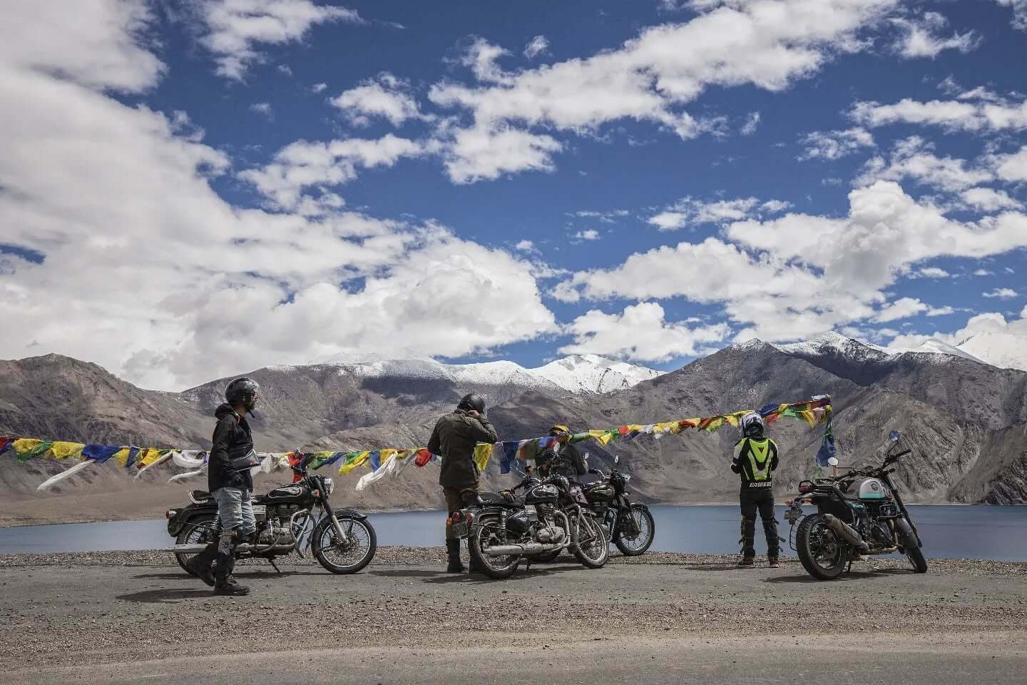 A high-altitude road cutting through a vast, barren desert landscape in Ladakh, with towering mountains and a car in the distance, emblematic of a road trip to Leh-Ladakh.