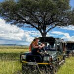 A jeep on a wildlife viewing track in the Maasai Mara National Reserve, surrounded by acacia trees and a large herd of animals, showcasing the best wildlife safari.
