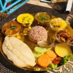 A group of friends sharing traditional Himachali food at a rustic outdoor cafe in Manali, surrounded by mountains, representing how group travel is the next big trend.