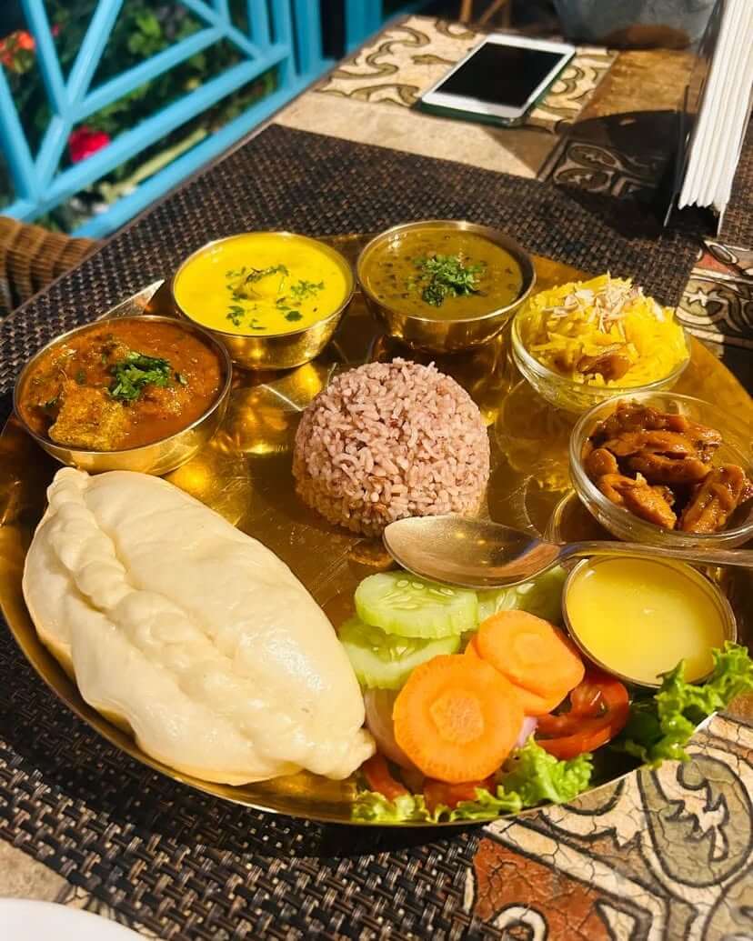 A group of friends sharing traditional Himachali food at a rustic outdoor cafe in Manali, surrounded by mountains, representing how group travel is the next big trend.