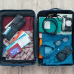 An organized, open suitcase with a variety of neatly packed clothes, shoes, and toiletries inside, placed on a wooden floor, ready for a trip.