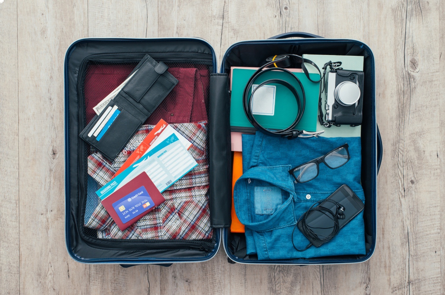 An organized, open suitcase with a variety of neatly packed clothes, shoes, and toiletries inside, placed on a wooden floor, ready for a trip.