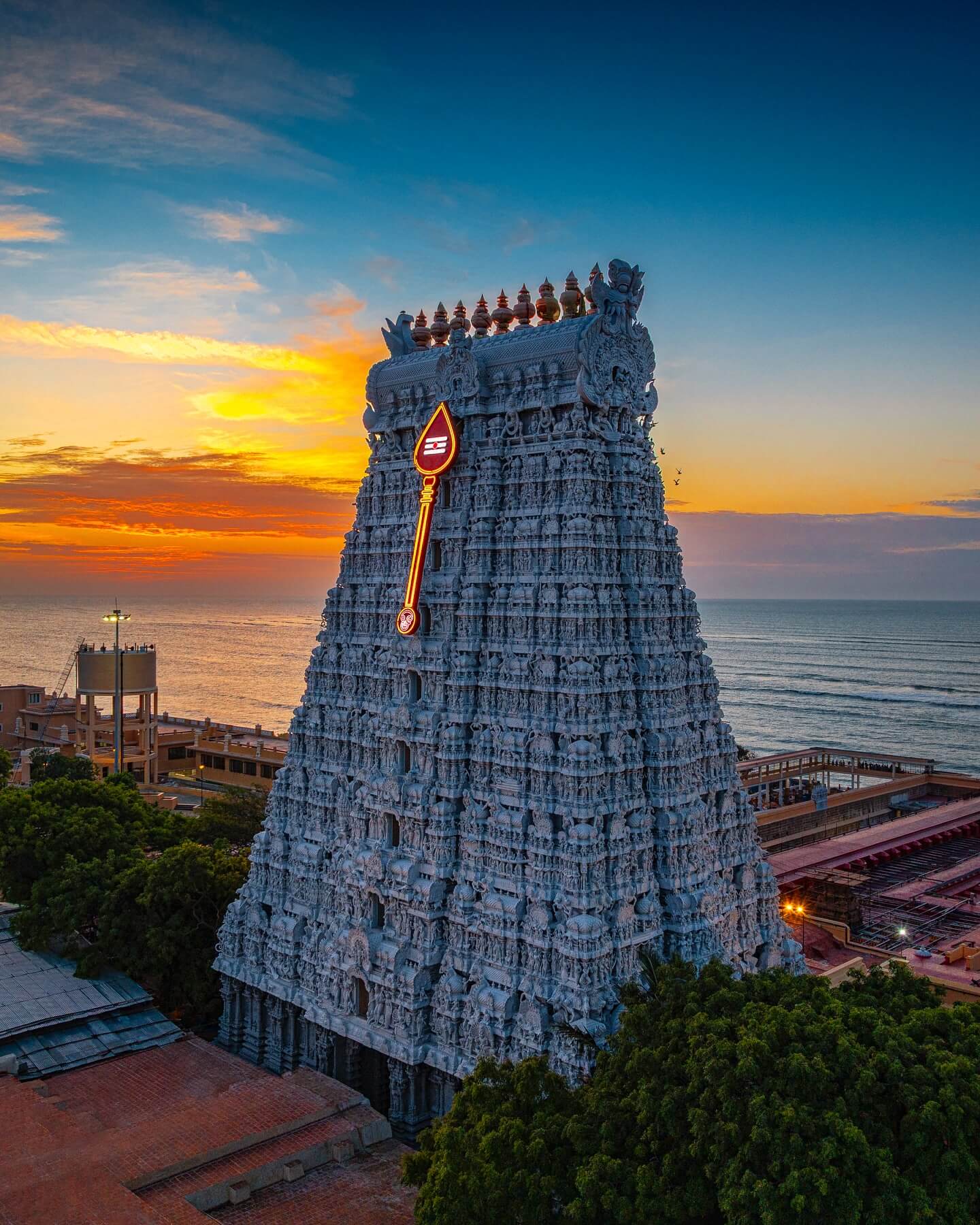 Alt Text A wide-angle, low-angle shot of the Meenakshi Amman Temple in Madurai, India, featuring a massive, tiered gopuram with countless intricate, colorful carvings of deities, figures, and animals under a bright blue sky.