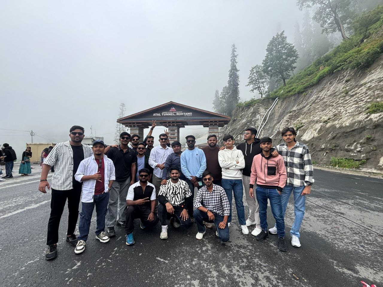 A scenic photograph of a group of friends trekking on a trail in the mountains of Manali, with lush green trees and snow-capped peaks in the distance.