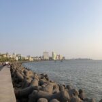 A high-angle, nighttime view of Marine Drive in Mumbai, showing the curved sea-facing promenade brilliantly lit up, resembling a 'Queen's Necklace.