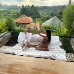 "Split image showing a couple enjoying a fun daytime activity on a Balinese beach on one side, and them having a private, romantic dinner under the stars at night on the other, representing a honeymoon holiday."