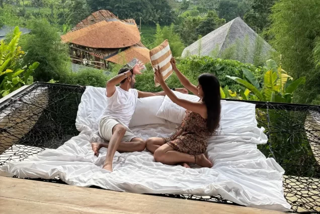 "Split image showing a couple enjoying a fun daytime activity on a Balinese beach on one side, and them having a private, romantic dinner under the stars at night on the other, representing a honeymoon holiday."