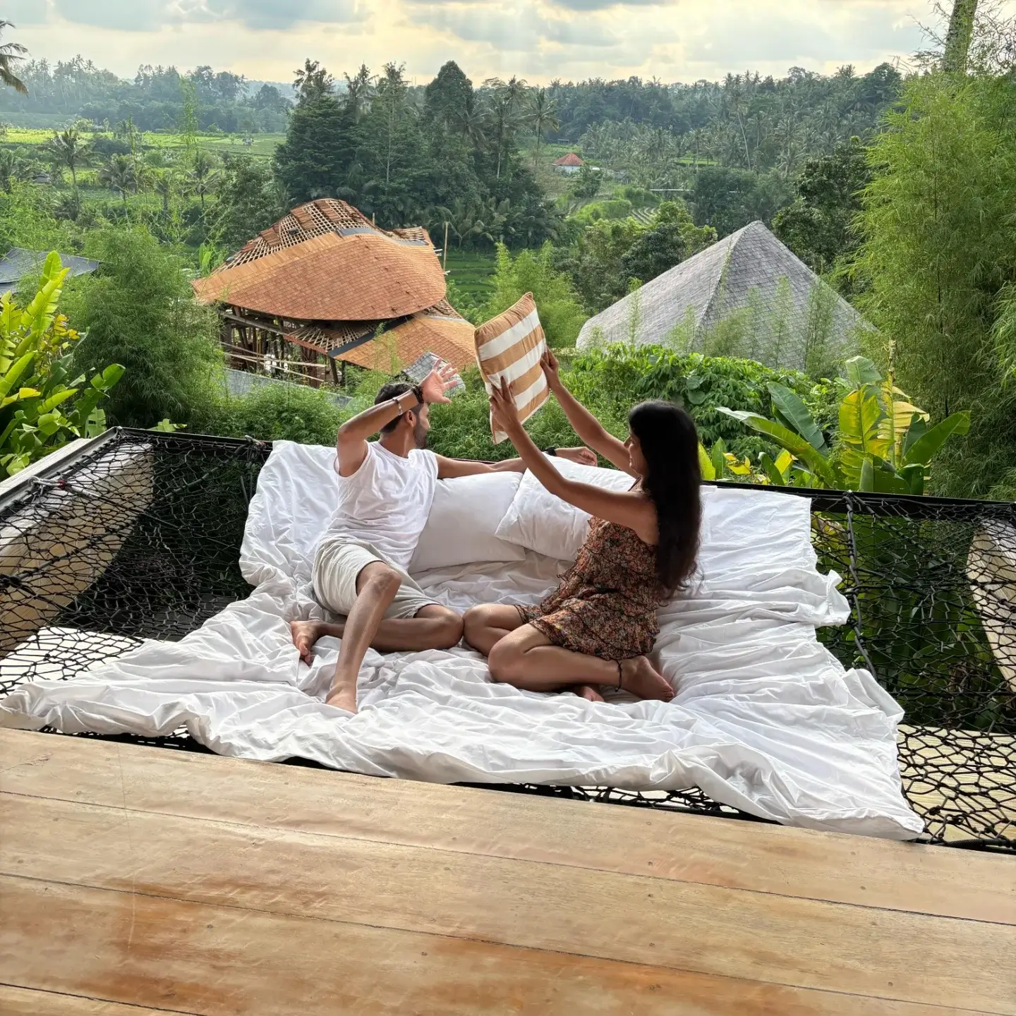 "Split image showing a couple enjoying a fun daytime activity on a Balinese beach on one side, and them having a private, romantic dinner under the stars at night on the other, representing a honeymoon holiday."
