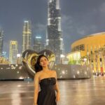 A panoramic photograph of the Burj Khalifa, the world's tallest building, at dusk, with the tower brightly lit and surrounded by the lights of the city and the Dubai Fountain in the foreground.