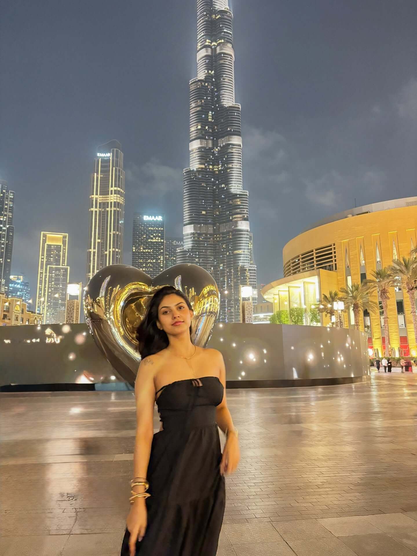 A panoramic photograph of the Burj Khalifa, the world's tallest building, at dusk, with the tower brightly lit and surrounded by the lights of the city and the Dubai Fountain in the foreground.
