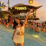 "The lively atmosphere of FINNS Beach Club, with people socializing around a large pool, enjoying cocktails at the bar, with a perfect view of the waves and beach."