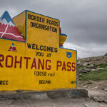 A scenic photograph of a winding road in the snowy mountains of Rohtang Pass, with snow-covered slopes and a clear sky, conveying a sense of high-altitude beauty and adventure.