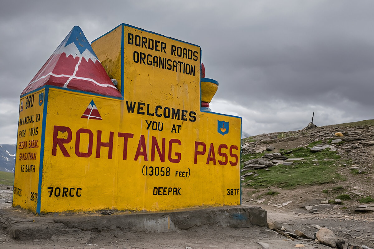 A scenic photograph of a winding road in the snowy mountains of Rohtang Pass, with snow-covered slopes and a clear sky, conveying a sense of high-altitude beauty and adventure.