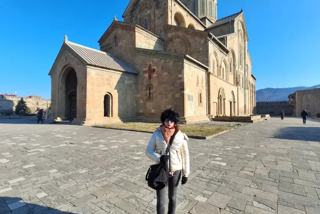 An exterior shot of the Svetitskhoveli Cathedral in Mtskheta, a large, historic stone cathedral with a prominent dome and an ornate facade, with people walking in the courtyard.