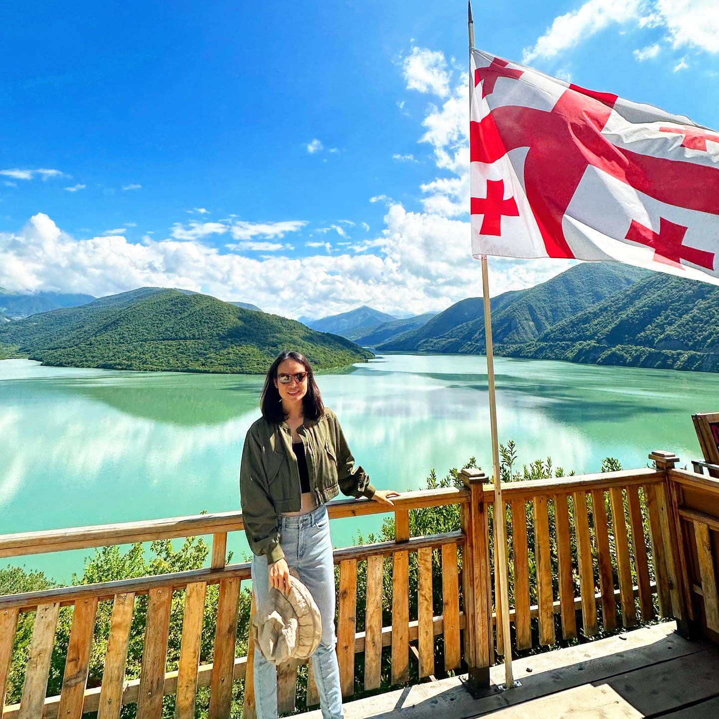 A panoramic photograph of the Zhinvali Reservoir, a large turquoise lake in Georgia, with a winding coastline and surrounding green mountains.