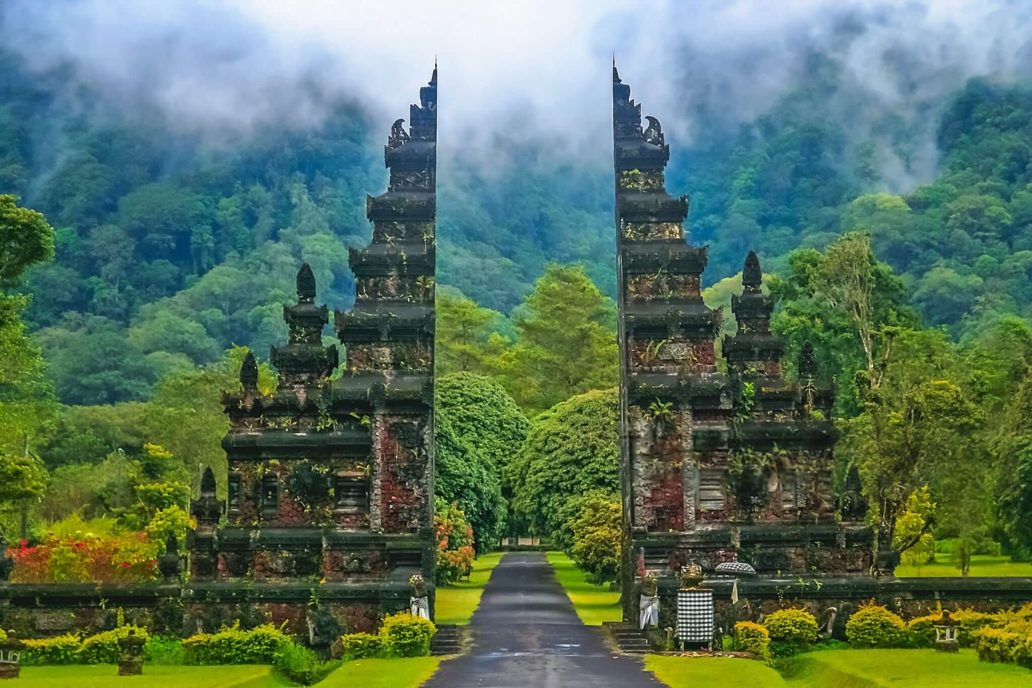 "A solo backpacker standing with a large backpack, looking out over vibrant green rice terraces in Ubud, Bali, under a clear sky."