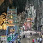 "A wide view of the vibrant 272-step rainbow staircase leading up to the main temple cave at Batu Caves, with the giant Lord Murugan statue standing sentinel."
