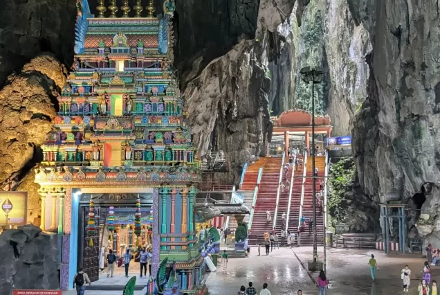 "A wide view of the vibrant 272-step rainbow staircase leading up to the main temple cave at Batu Caves, with the giant Lord Murugan statue standing sentinel."