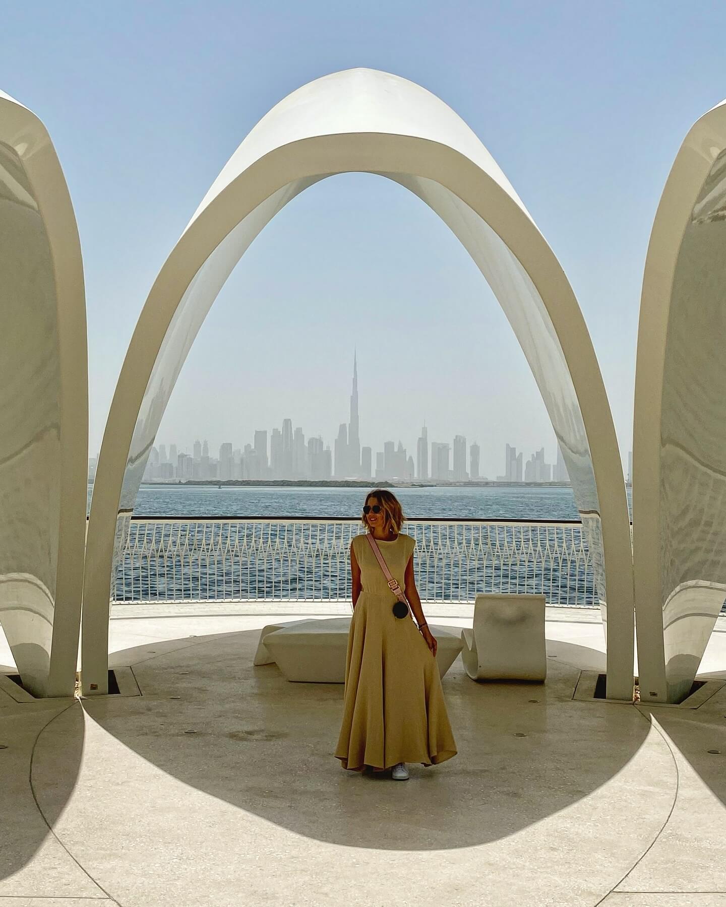 An exterior shot of Dubai Creek, a waterway filled with traditional wooden boats, with a view of the city's historical buildings and the modern skyline in the distance.