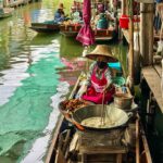 "Colorful boats filled with tropical fruits, vegetables, and street food at a traditional Thai floating market, with vendors interacting with customers on the water and along the banks."