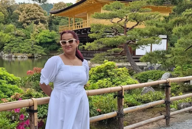 The Golden Pavilion, or Kinkaku-ji, is a brilliant gold-leaf-covered Zen Buddhist temple, standing on the edge of a serene pond, surrounded by lush gardens under a clear sky.