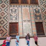 An exterior photograph of the Palace of Sheki Khans, a historic summer palace in Sheki, Azerbaijan, showing its ornate facade with stained-glass windows and intricate decorative carvings.
