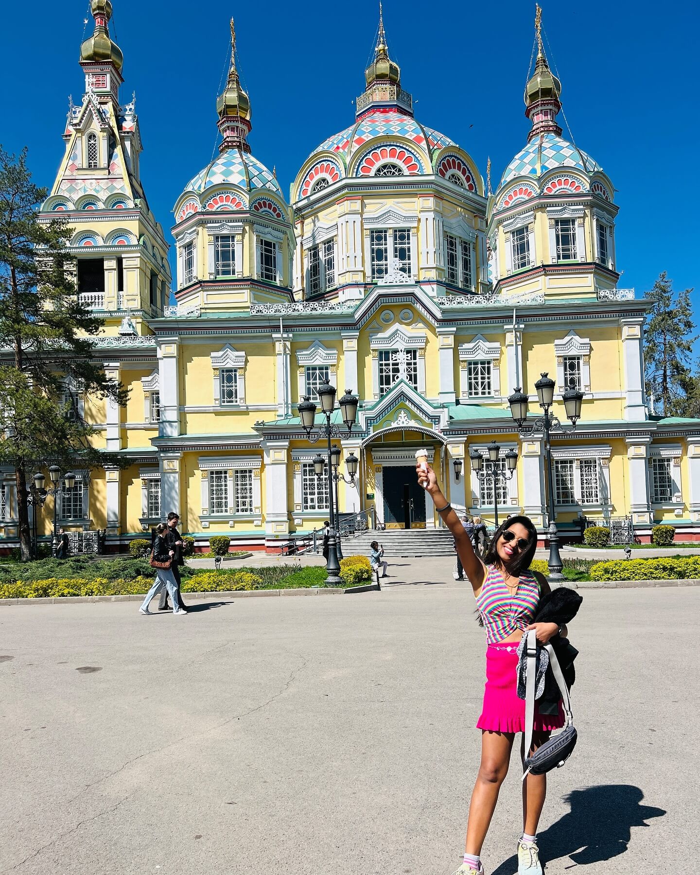 A photograph of the Zenkov Cathedral, a bright yellow and green Russian Orthodox cathedral made of wood, set against a backdrop of trees in a park.