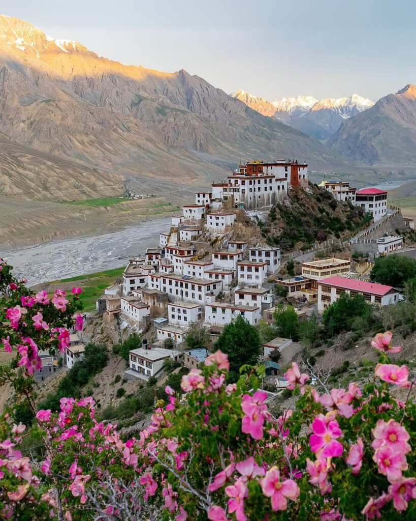 An exterior shot of Key Monastery, a large, multi-level Buddhist monastery perched on a hilltop in Spiti Valley, surrounded by barren, high-altitude mountains under a clear sky.