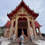 A wide shot of Wat Chalong, a prominent Buddhist temple in Phuket, Thailand, featuring ornate golden and red roofs, intricate carvings, and statues, set against a clear sky.