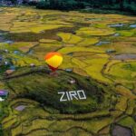 A panoramic view of the Ziro Valley in Arunachal Pradesh, showcasing its terraced paddy fields and a small village surrounded by lush green hills.