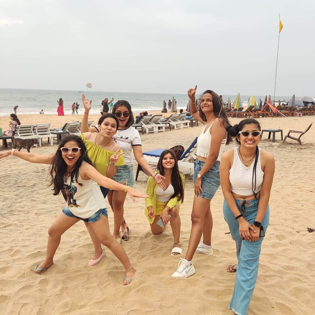A rocky coastline with the sun setting over the Arabian Sea, showing a few people on the beach and the distinct black rock formations that are characteristic of Anjuna Beach in Goa.