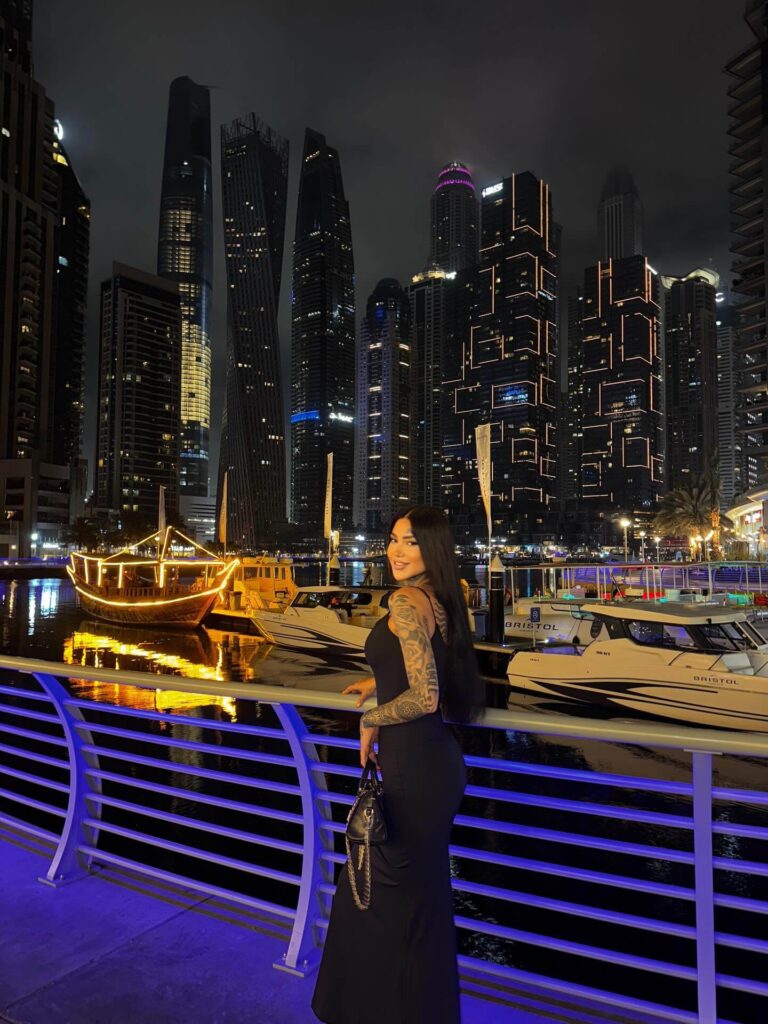 A photograph of a group of people on a yacht in Dubai Marina at night, with the illuminated skyline of the city in the background.