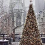 An exterior shot of the Rockefeller Center in New York City during Christmas, showing the iconic ice-skating rink, the large, decorated Christmas tree, and the surrounding buildings illuminated with festive lights.