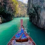 A scenic photograph of a beautiful beach in Thailand, with a traditional longtail boat on the turquoise water and a backdrop of green, limestone cliffs. Best to Visit in January