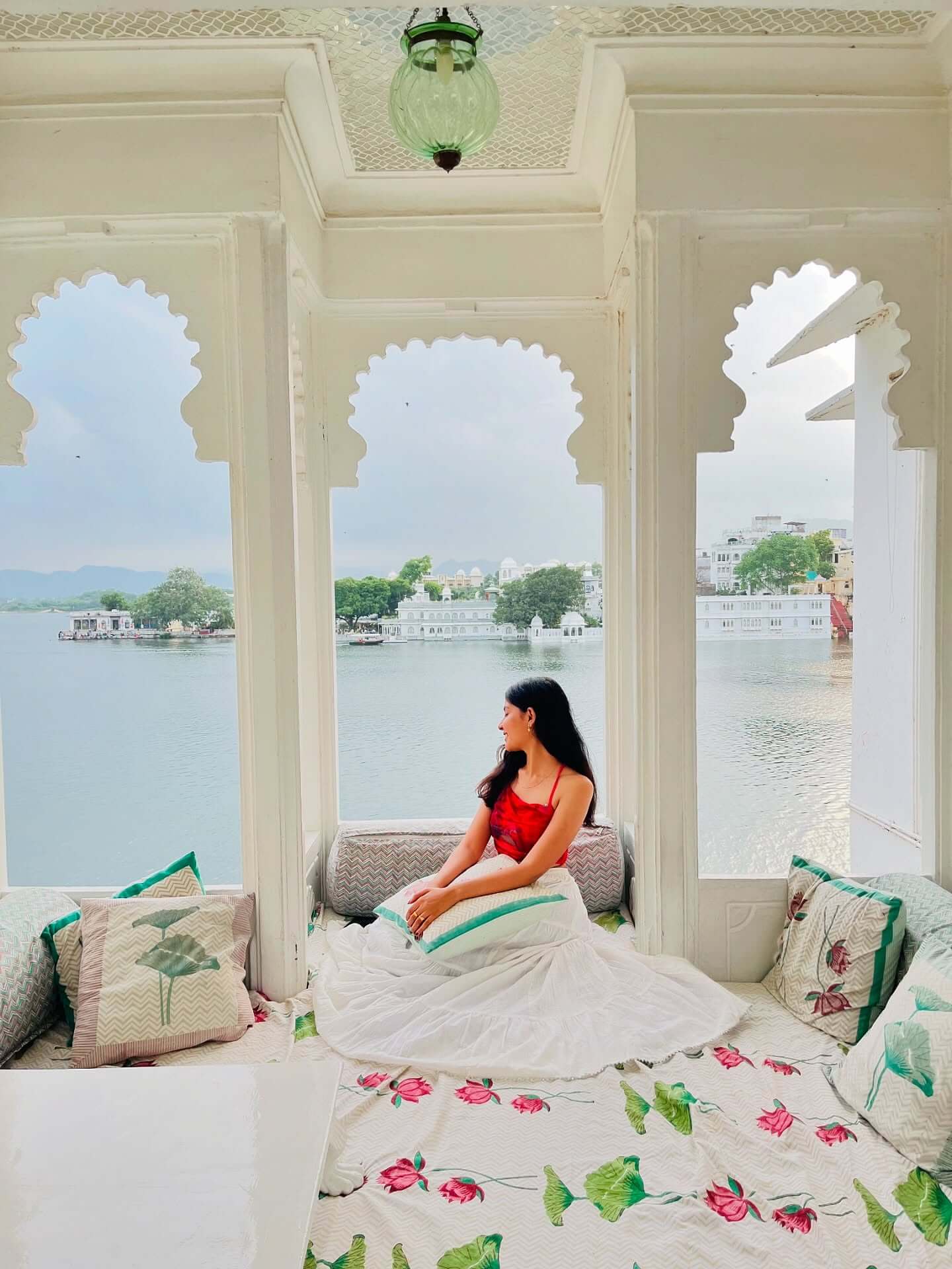 A photograph of the exterior of the City Palace in Udaipur, a grand and ornate structure on the banks of a lake, with a bright blue sky and a few boats visible on the water.