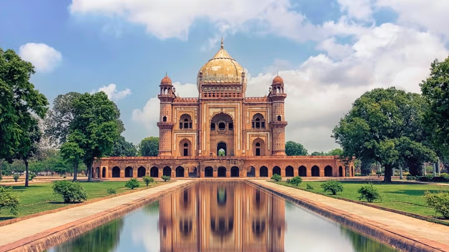 An exterior shot of the Hawa Mahal in Jaipur, a historic red and pink sandstone palace with a honeycomb facade of small windows, standing on a bustling street.