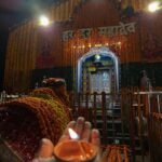 The front facade of Kedarnath Temple during a heavy snowfall, featuring the "Jai Shree Kedar" sign and a snow-covered Nandi statue.