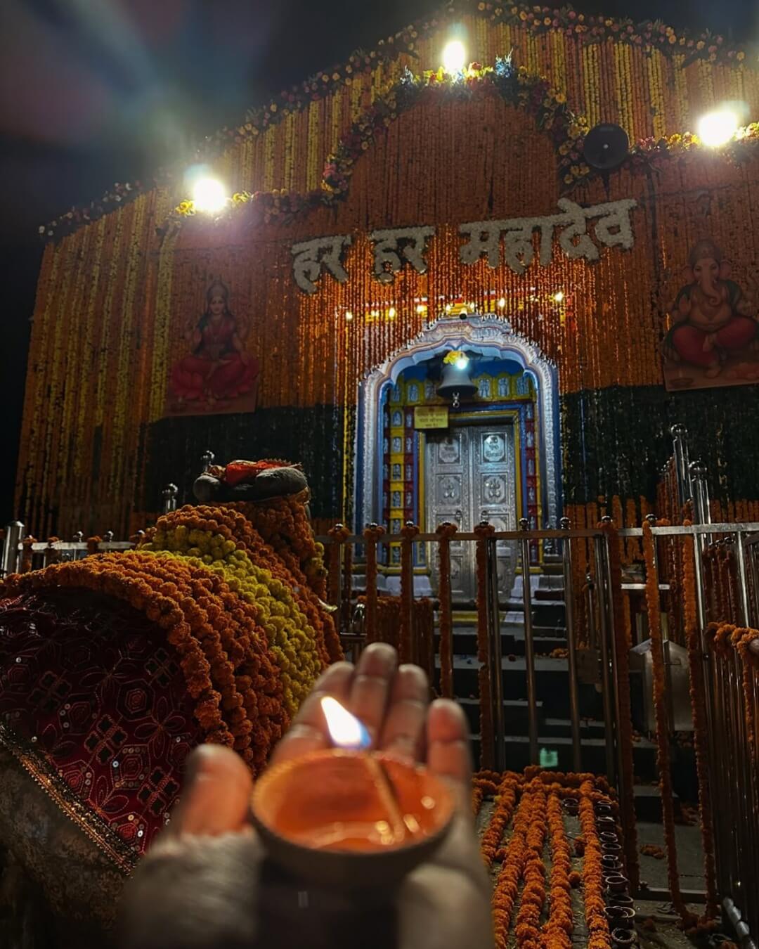 The front facade of Kedarnath Temple during a heavy snowfall, featuring the "Jai Shree Kedar" sign and a snow-covered Nandi statue.