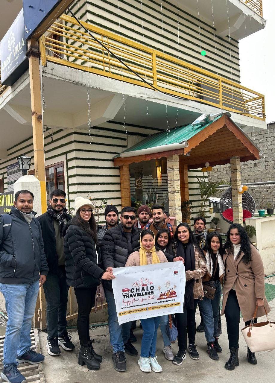 A group of young pilgrims posing with a "Chalo Travellers" banner in front of the Amrit Villa guest house, dressed in heavy winter jackets and beanies. Republic Day LongWeekend Group Trip From Delhi