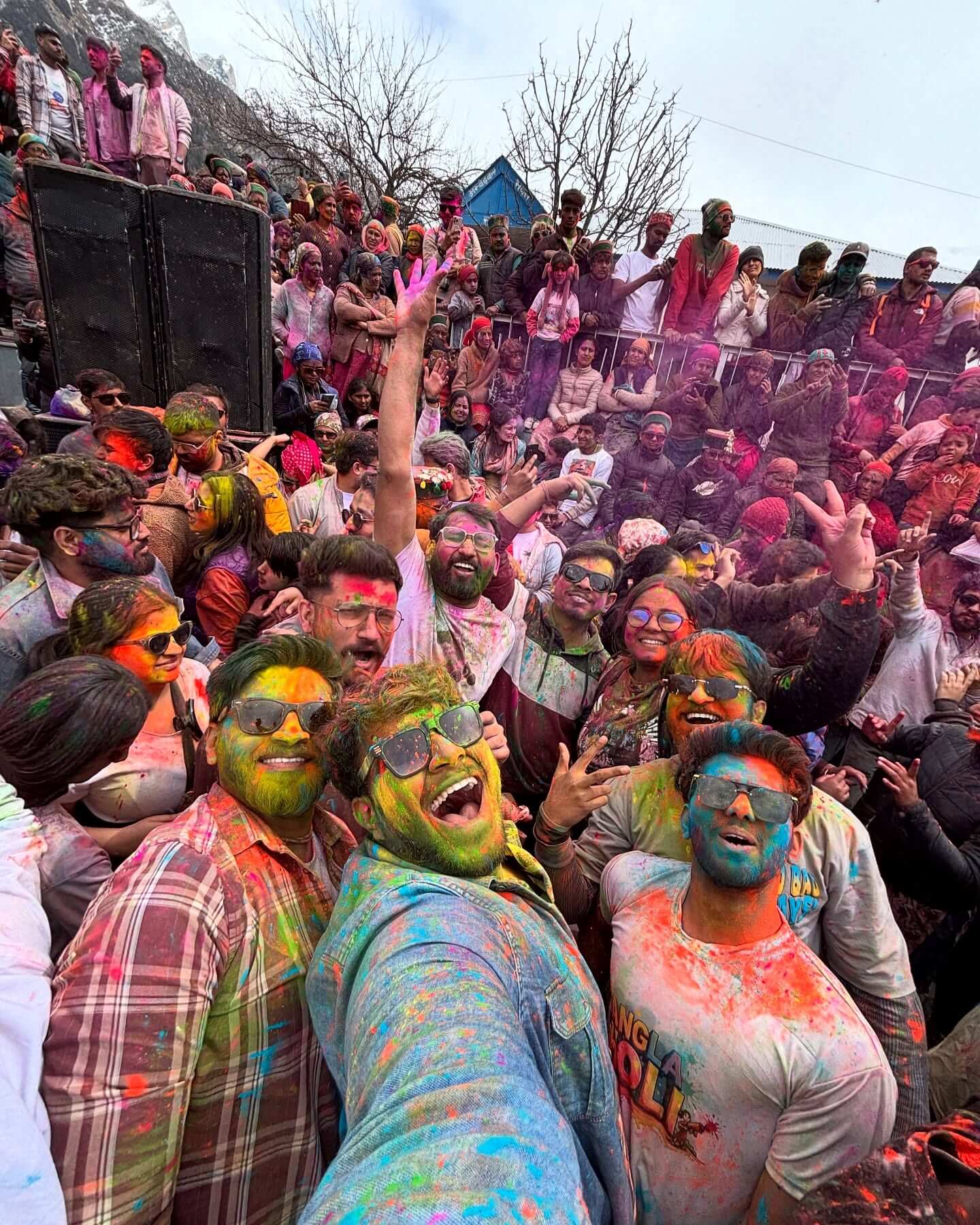 Travelers celebrating vibrant Holi during the Faguli Festival in Sangla Valley with snow-capped Himalayan mountains in the background – Chalo Travellers Sangla Holi Road Trip 2026.