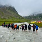 River crossing during Hampta Pass trek with hikers walking through water