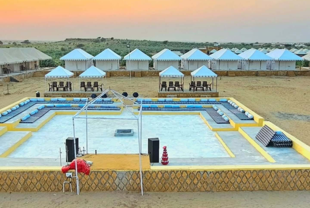 Luxury desert camps set against the golden sand dunes of Sam, Jaisalmer during sunset with camels in the foreground.